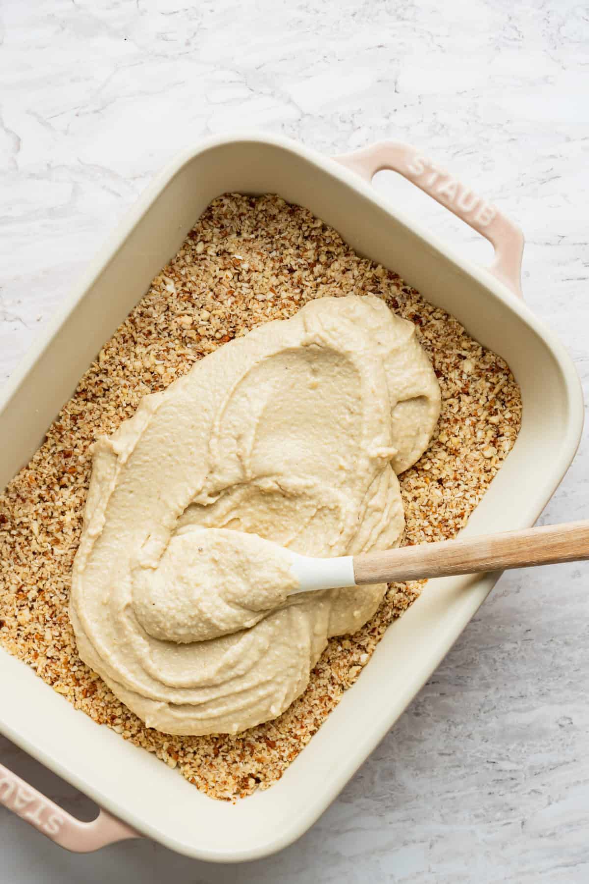A pan with a crust in it with a thick white mixture being spread on top of it.