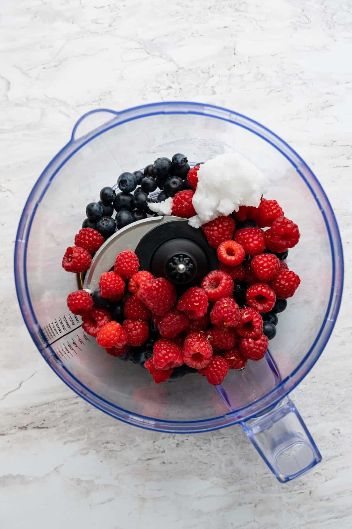 A blender with raspberries, blueberries and coconut milk in it.