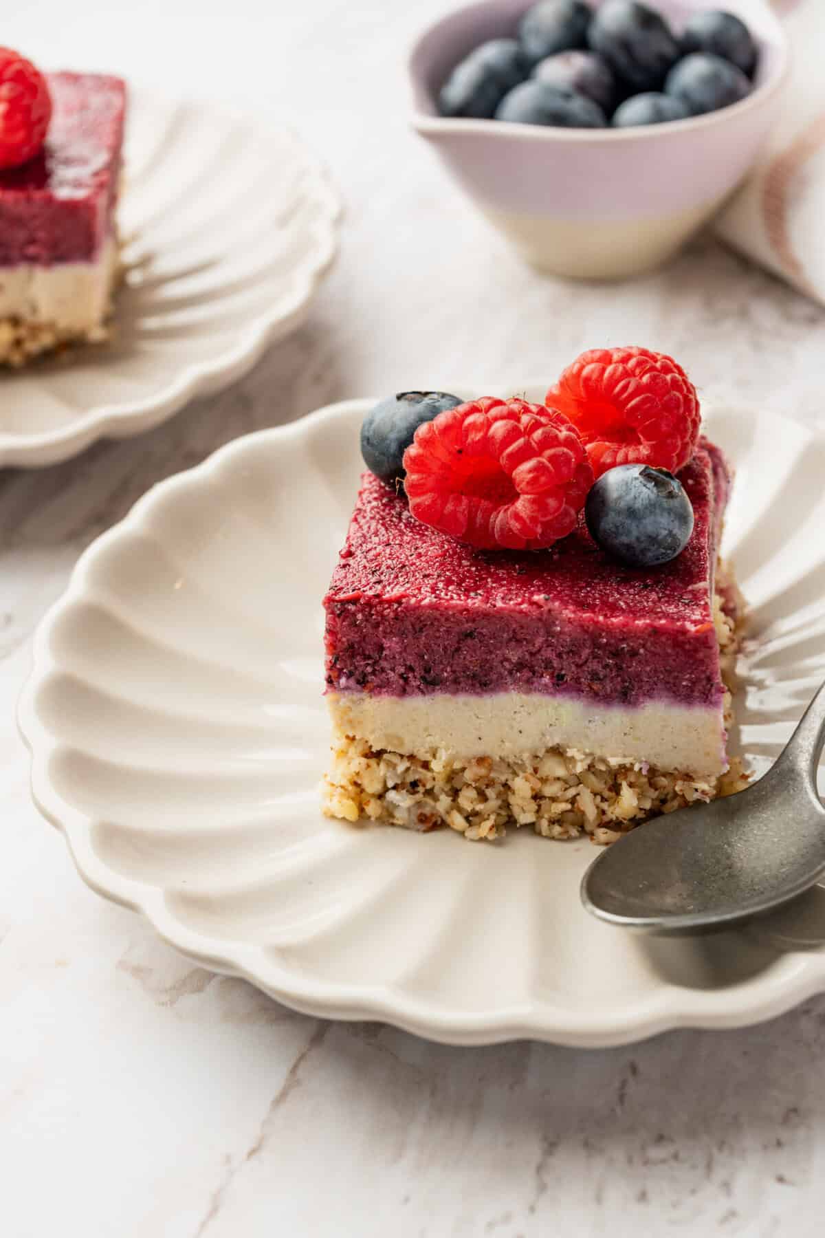 A dessert bar with a crumble layer, a white layer and a pink layer on a plate.