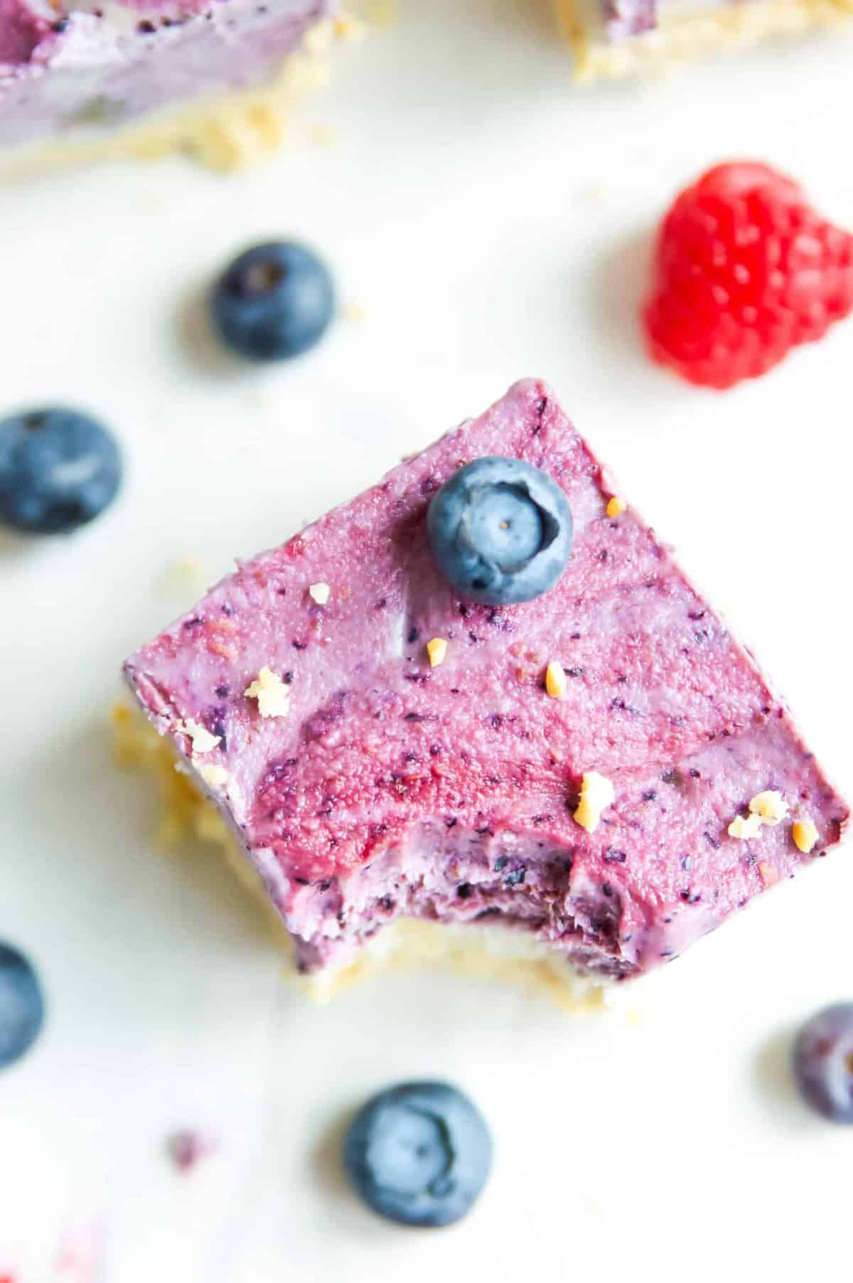 A berry ice cream bar with a bite out of it and a blueberry on top.