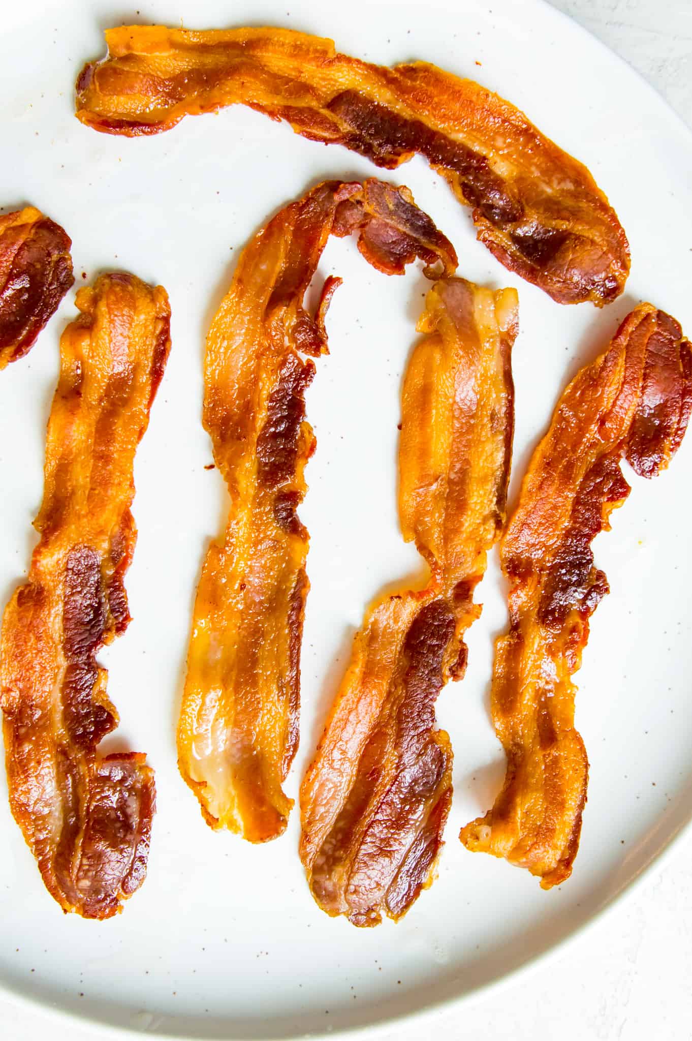 A plate full of cooked bacon strips.