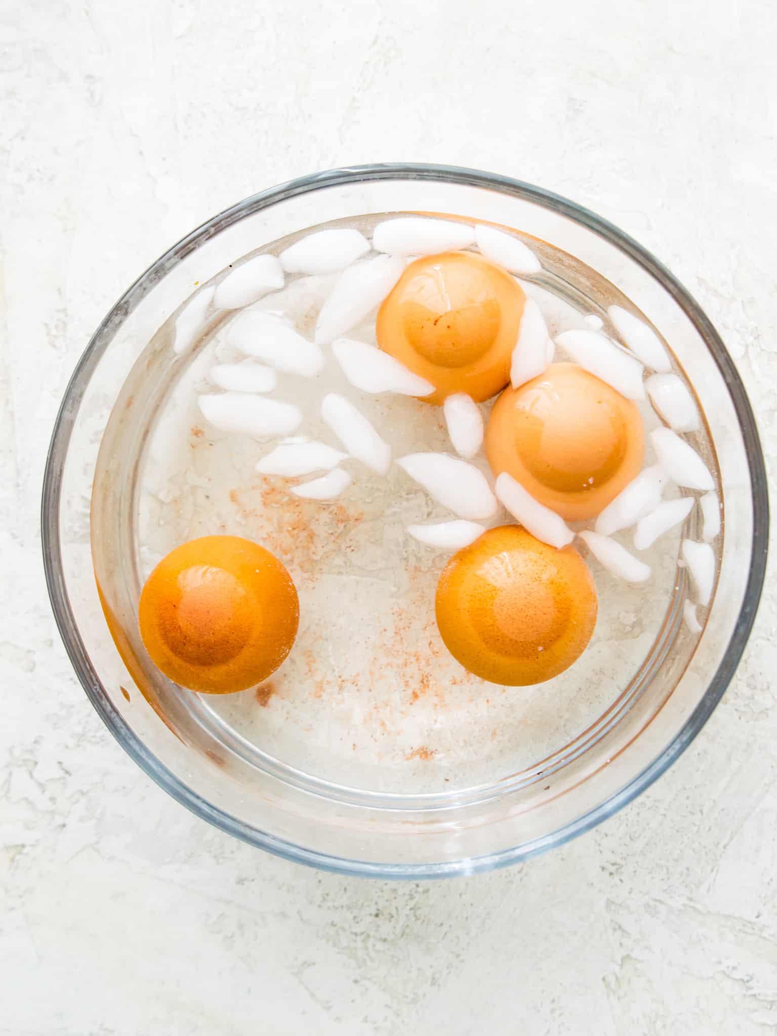 A clear glass bowl filled with water, ice cubes and four eggs.