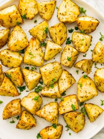A plate of cooked, diced potatoes garnished with fresh parsley.