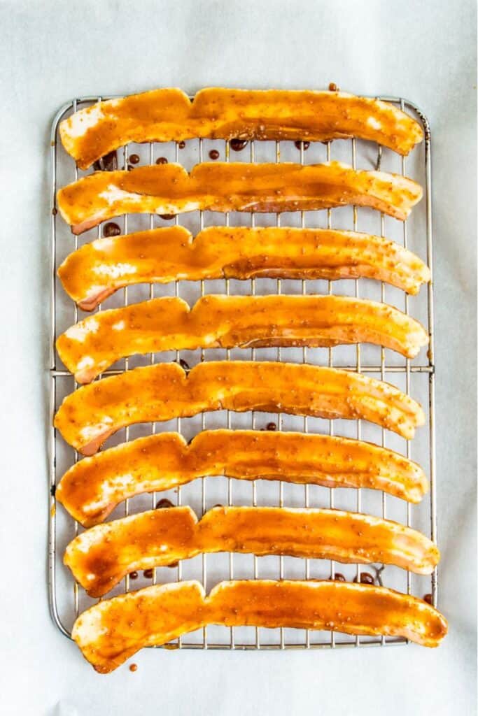 Strips of bacon coated in a sugar mixture on a baking rack lined with parchment paper.