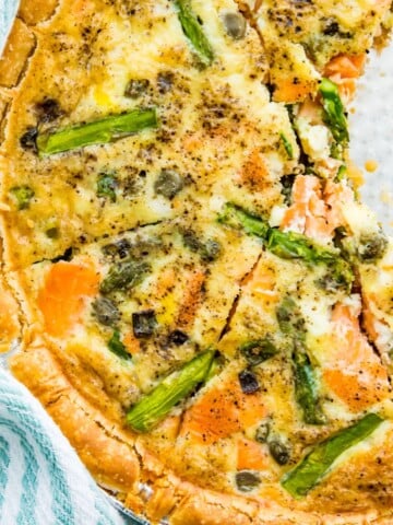 A smoked salmon and asparagus quiche cut into pieces in a pie plate.