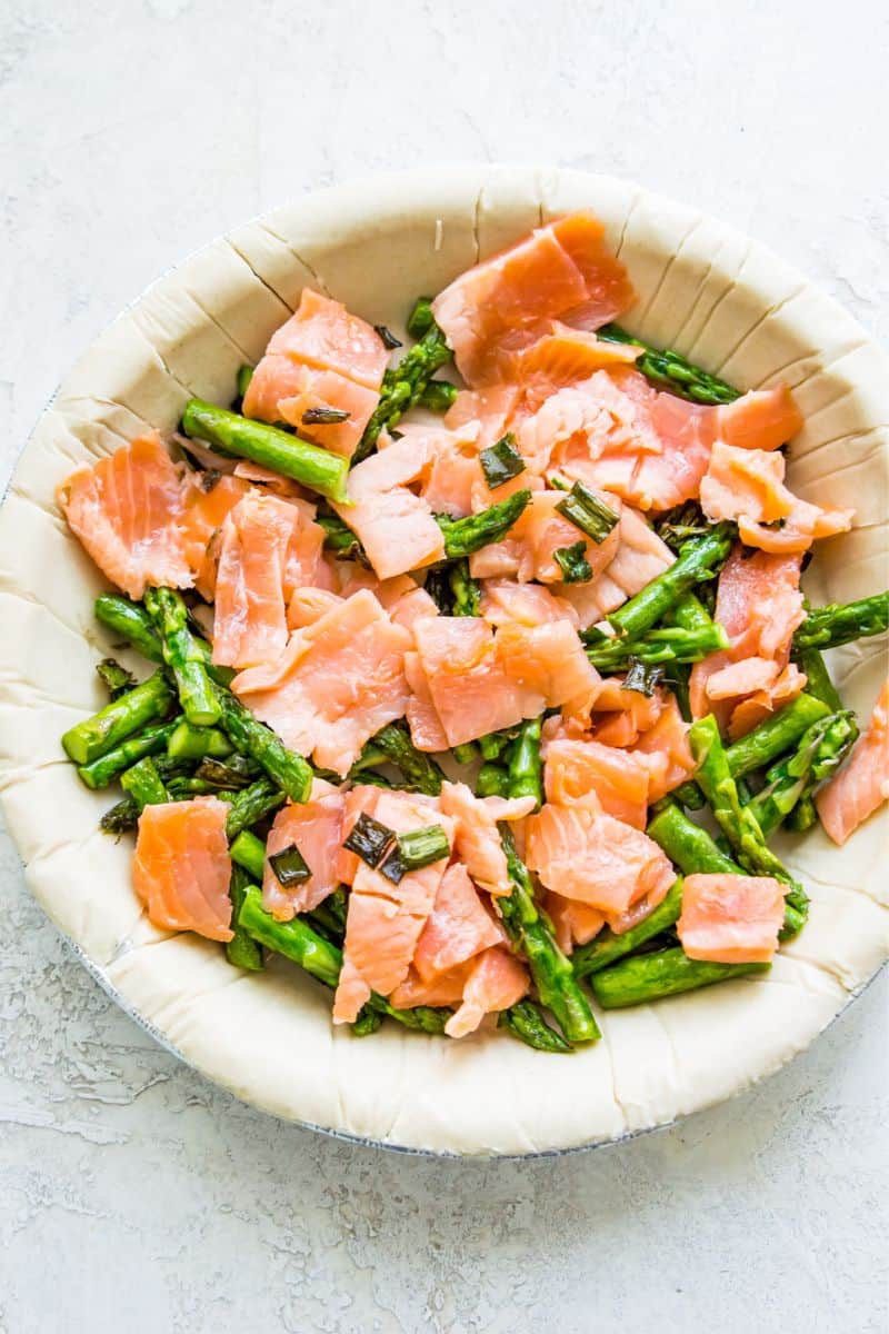 A pie crust filled with chopped smoked salmon, chopped asparagus and green onion.