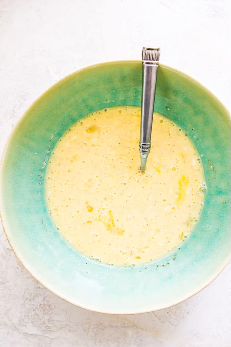 A bowl filled with whisked eggs and a spoon in it.