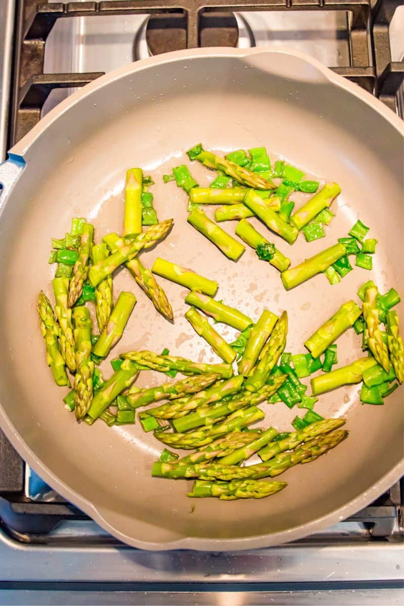 A pan on the stovetop with chopped asparagus and green onion in it.