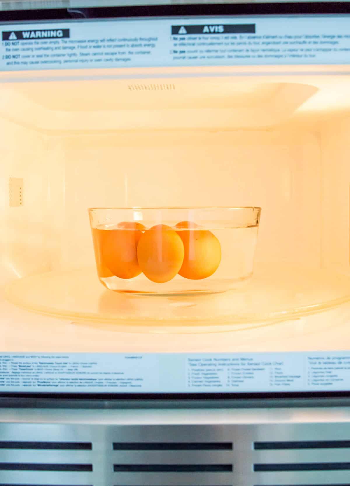 A clear glass bowl in a microwave filled with four eggs and water.
