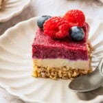 A dessert bar with a crumble layer, white layer and pink layer on a plate.