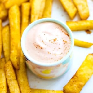 A small bowl of vegan sriracha mayo with French fries around it.