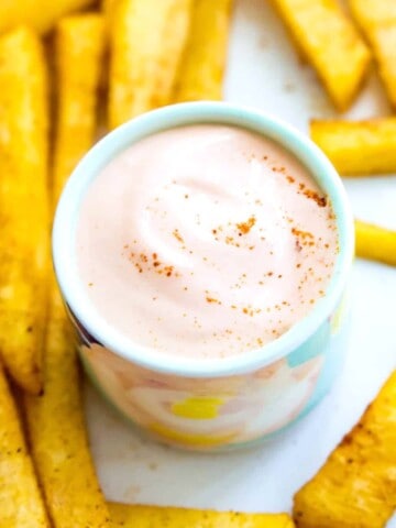 A small bowl of vegan sriracha mayo with French fries around it.