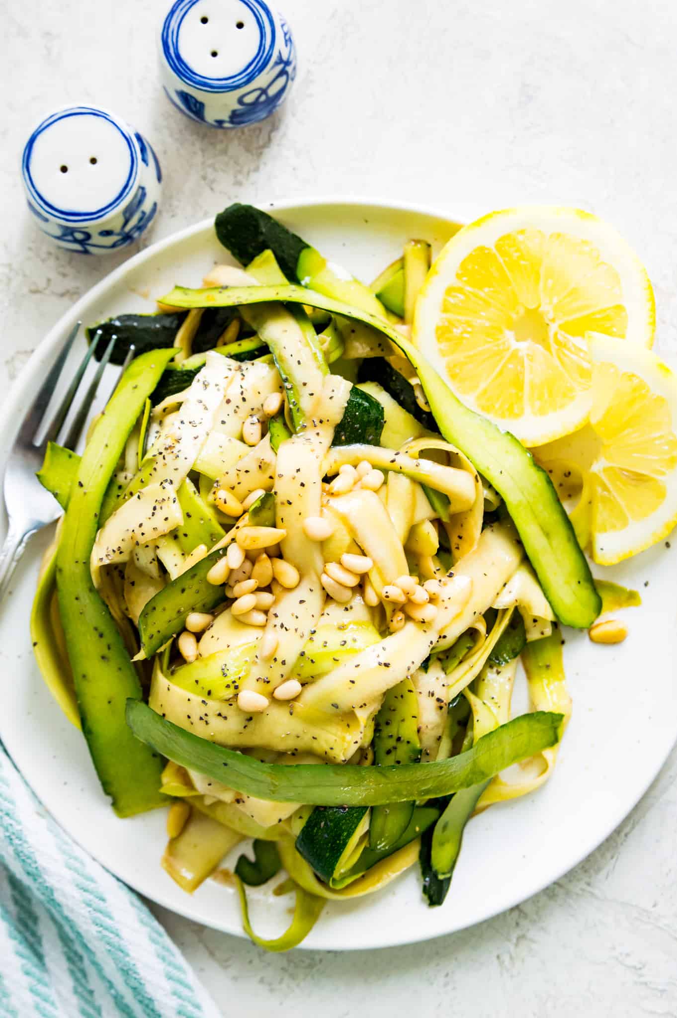 A raw courgette salad on a plate with lemon wedges