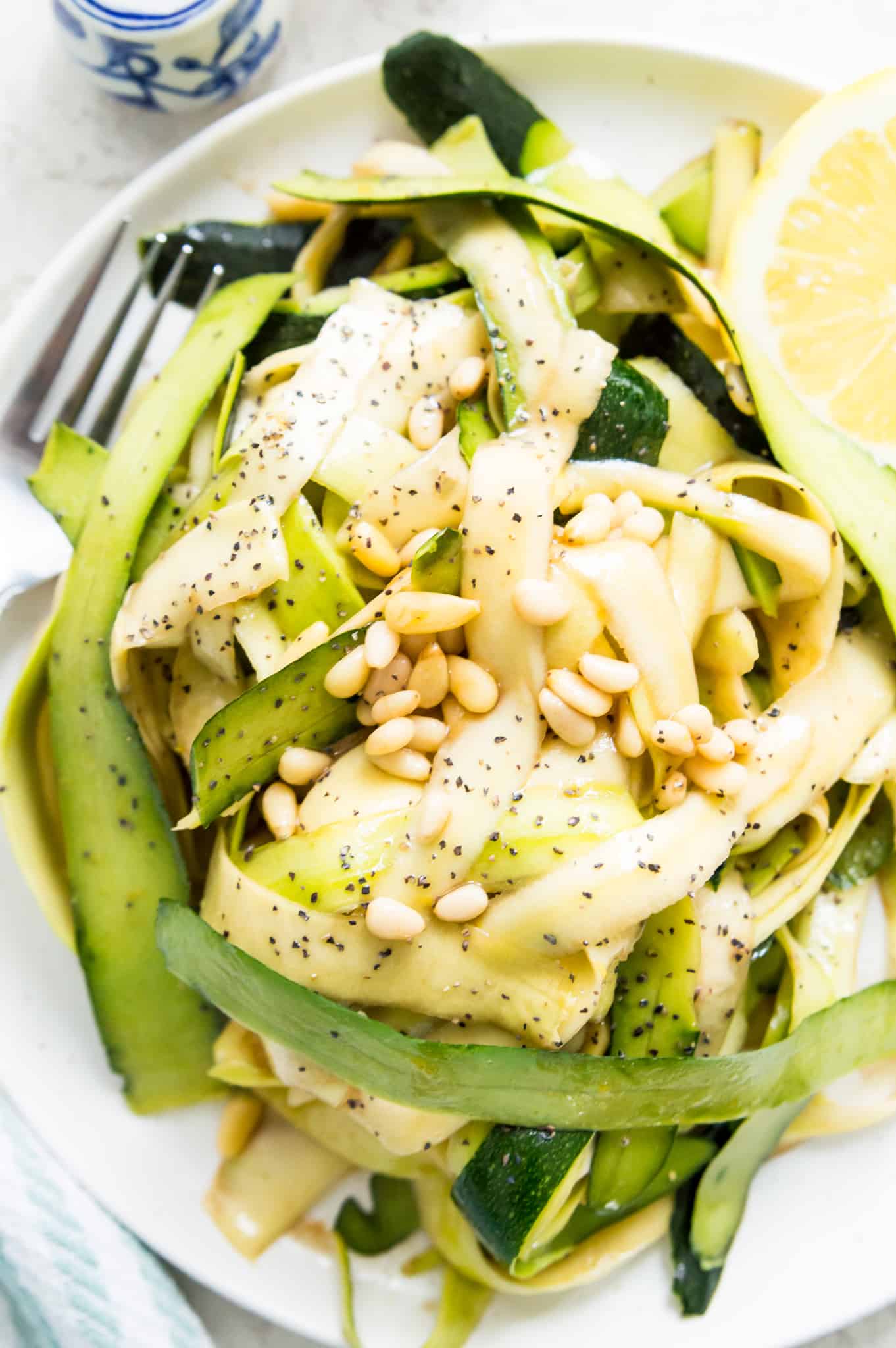 A raw zucchini salad on a plate topped with pine nuts.