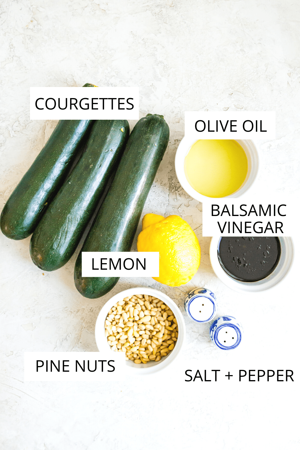 The ingredients needed for making a courgette salad including zucchinis, pine nuts, balsamic vinegar, oil and lemon.