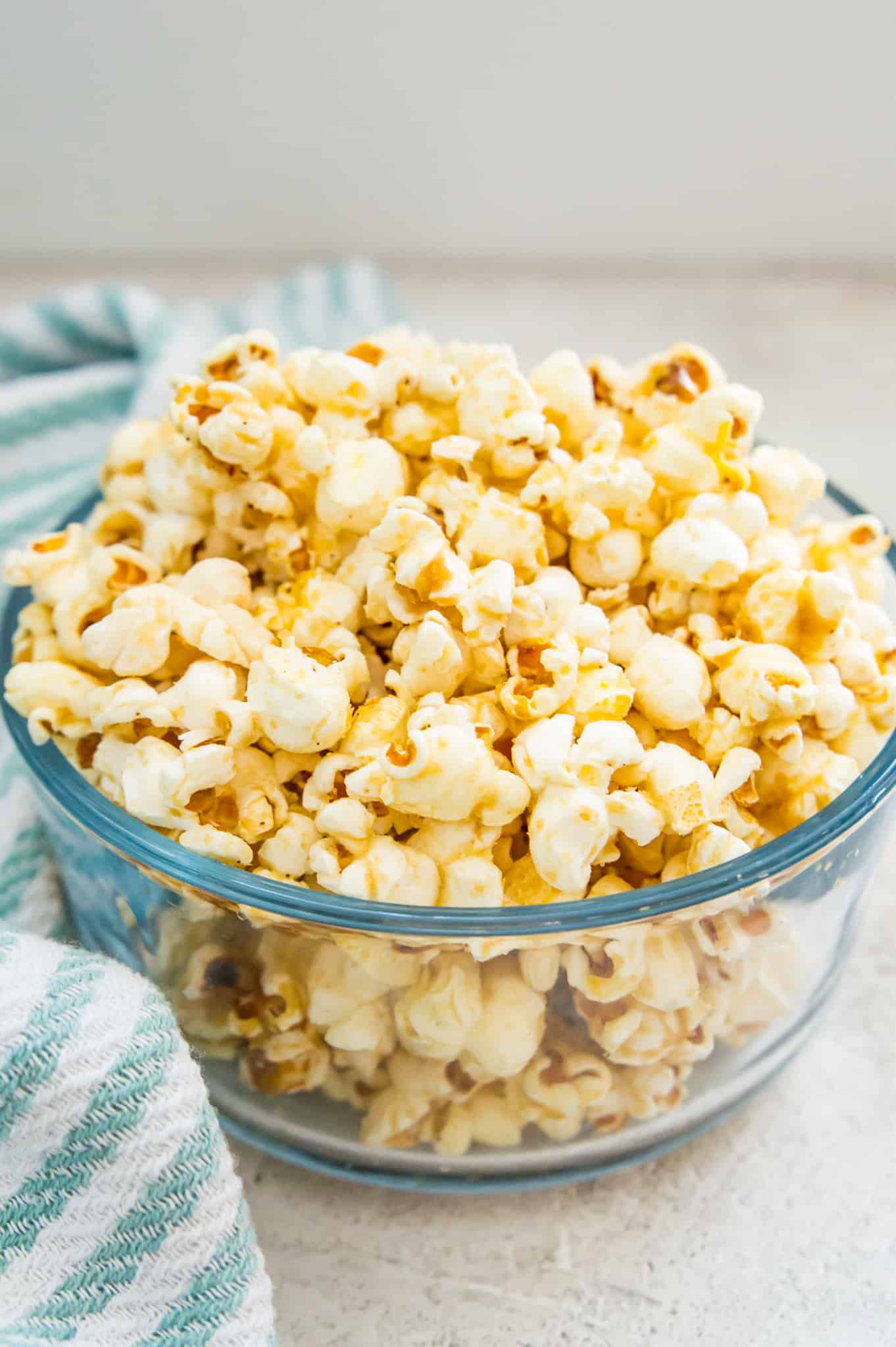 A bowl of dairy free popcorn with a tea towel beside it.