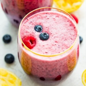 A glass of berry lemonade smoothie topped with fresh blueberries and raspberries.