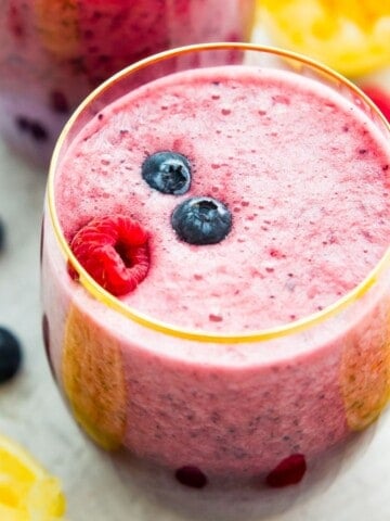 A glass of berry lemonade smoothie topped with fresh blueberries and raspberries.