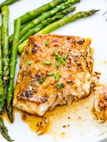 A piece of blackened cod on a plate with cooked asparagus.