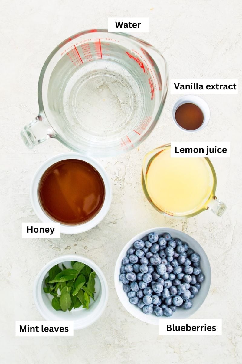 The ingredients needed for making blueberry mint lemonade separated into bowls including lemon juice, blueberries, mint leaves, water and honey.