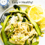 A raw zucchini salad on a plate with lemon wedges