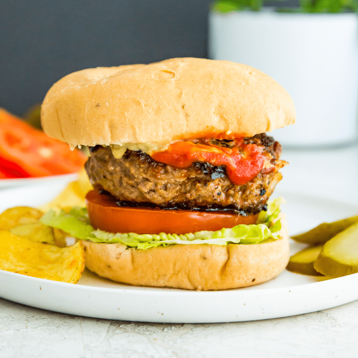 Homemade gluten free burger on a bun on a plate with a side of chips and pickles.