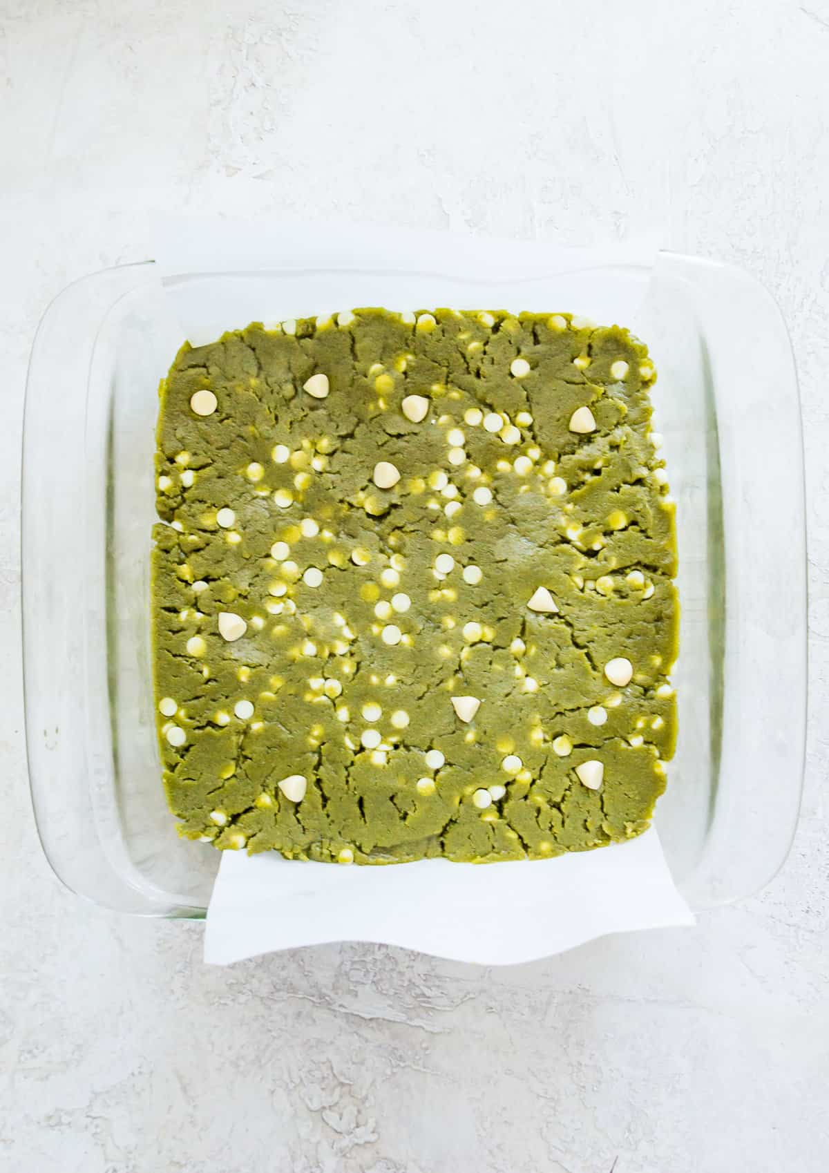 A glass baking dish lined with parchment paper with a green brownie batter in it.
