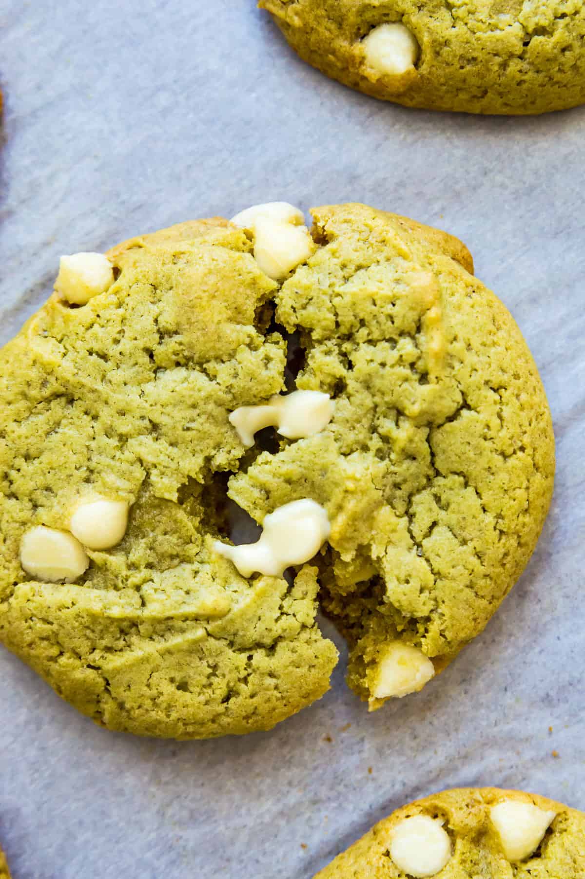 Matcha cookies with white chocolate chips on a piece of parchment paper.
