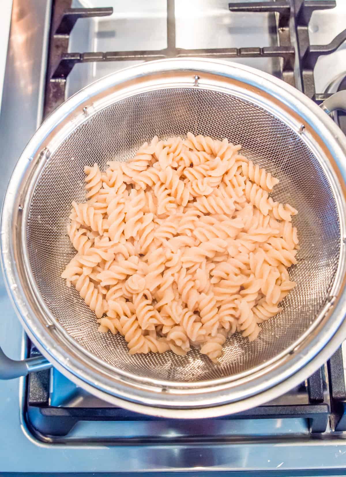 A metal colander with cooked spiral noodles in it.