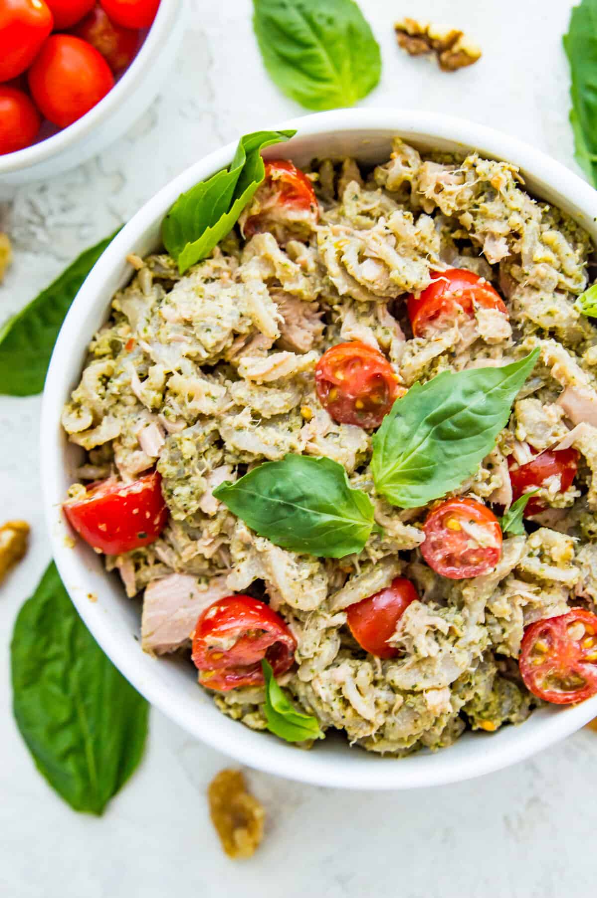 A bowl of tuna pasta pesto topped with fresh  basil leaves.