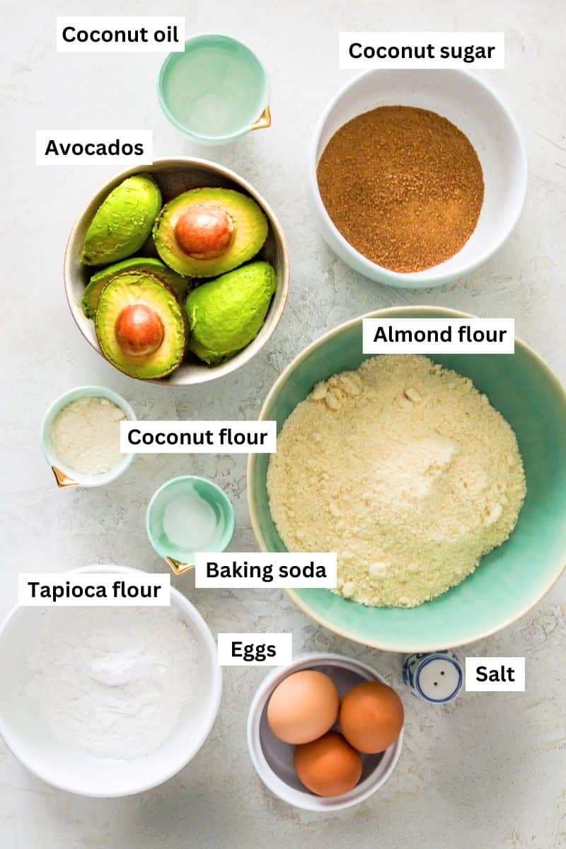 The ingredients for making avocado bread separated into bowls including flour, sugar, avocados, eggs and baking soda.