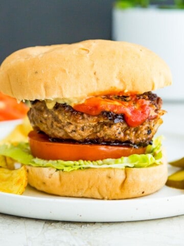 A gluten free burger in a bun with lettuce, tomato and ketchup.