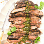 cut bavette steak on a platter with chimichurri sauce