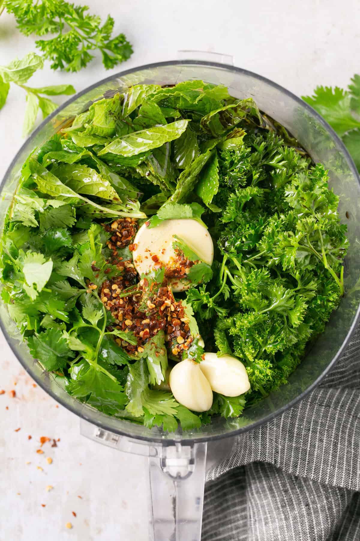 A food processor with nay different fresh herbs in it.