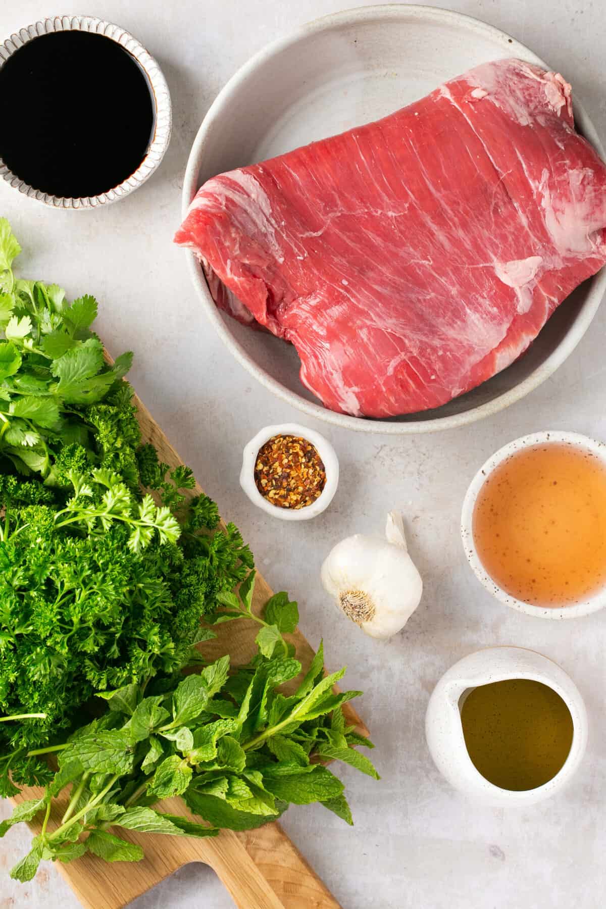 Ingredients needed for making bavette steak and chimichurri sauce including fresh herbs, garlic, olive oil and balsamic vinegar.