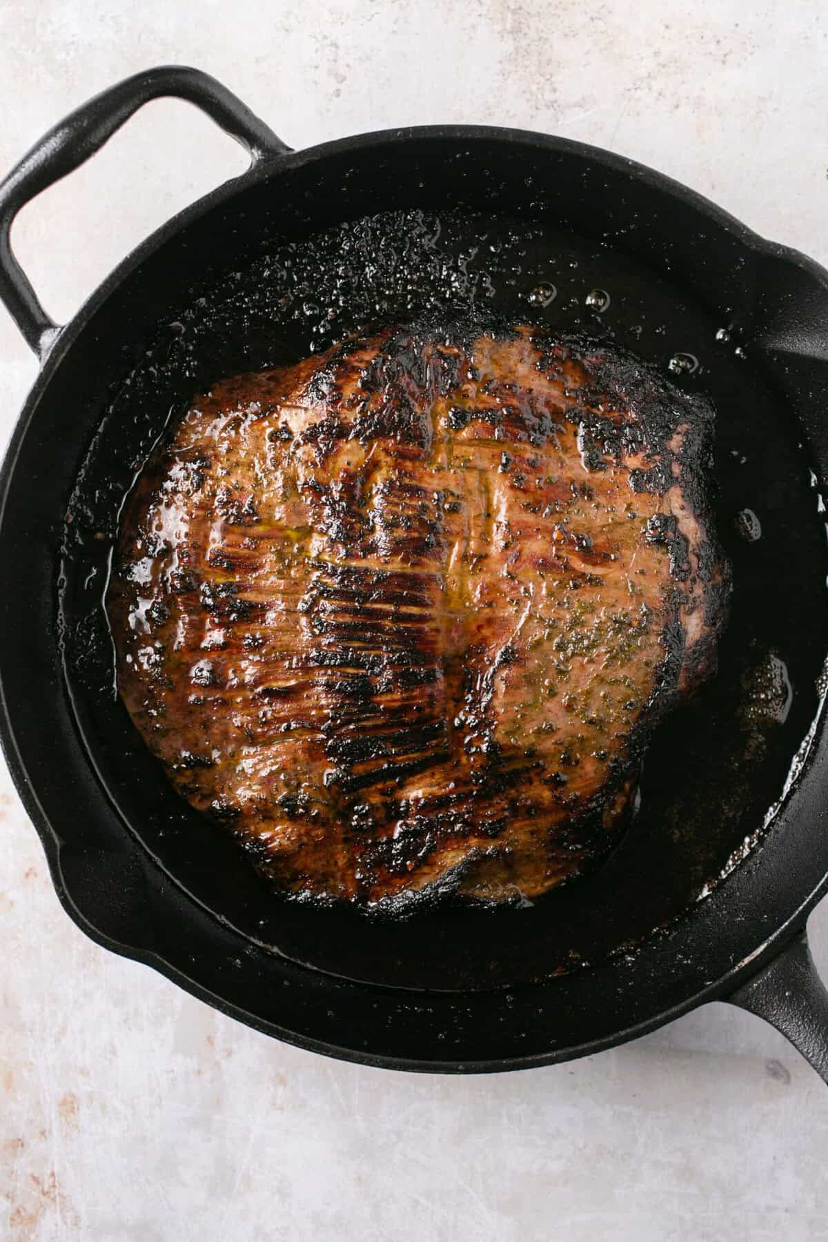 A piece of steak cooking in a cast iron skillet.