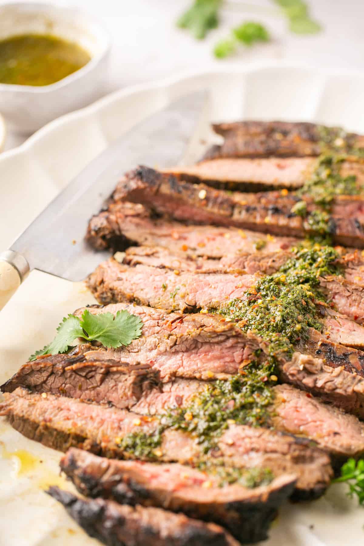 cut flank steak on a platter with chimichurri