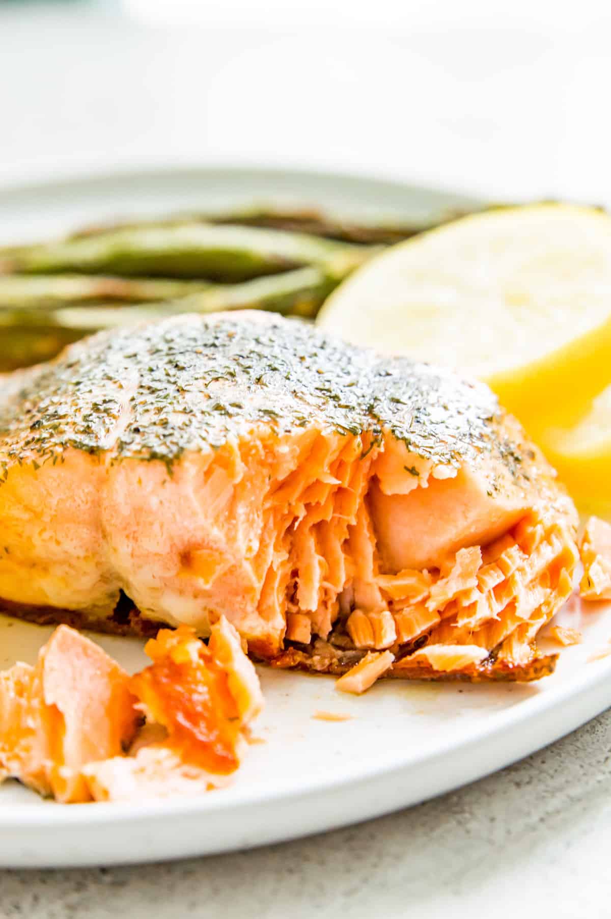 A piece of cooked salmon on a plate with asparagus and lemon slices.