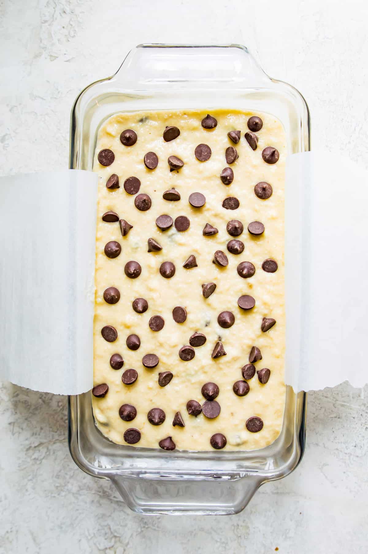 A glass loaf pan with batter in it topped with chocolate chips.