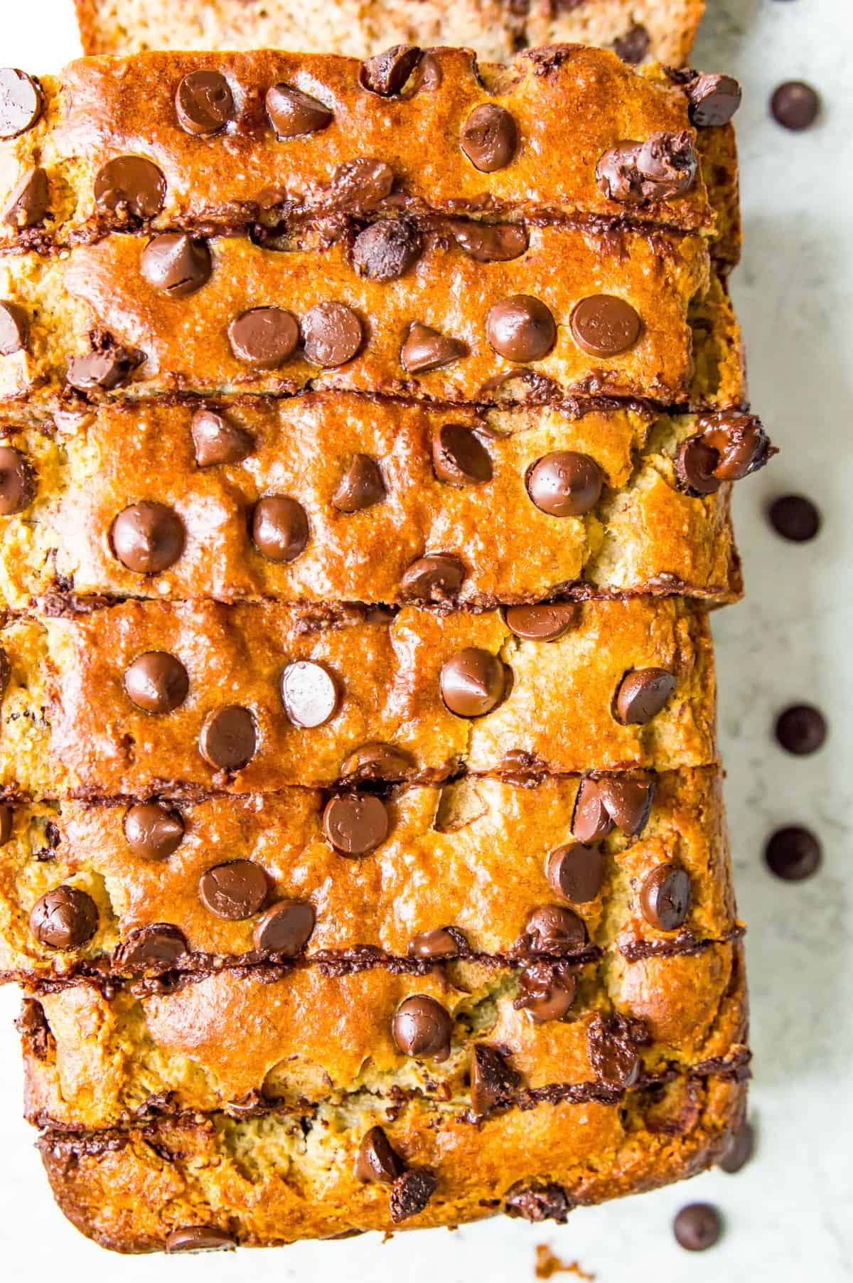 A loaf of chocolate chip banana bread cut into pieces with chocolate chips around it.