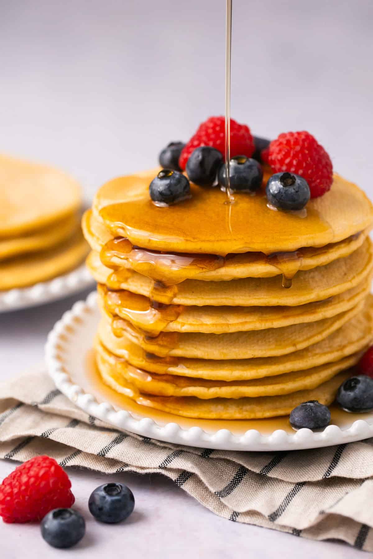 A stack of oat milk pancakes with maple syrup and berries on top.