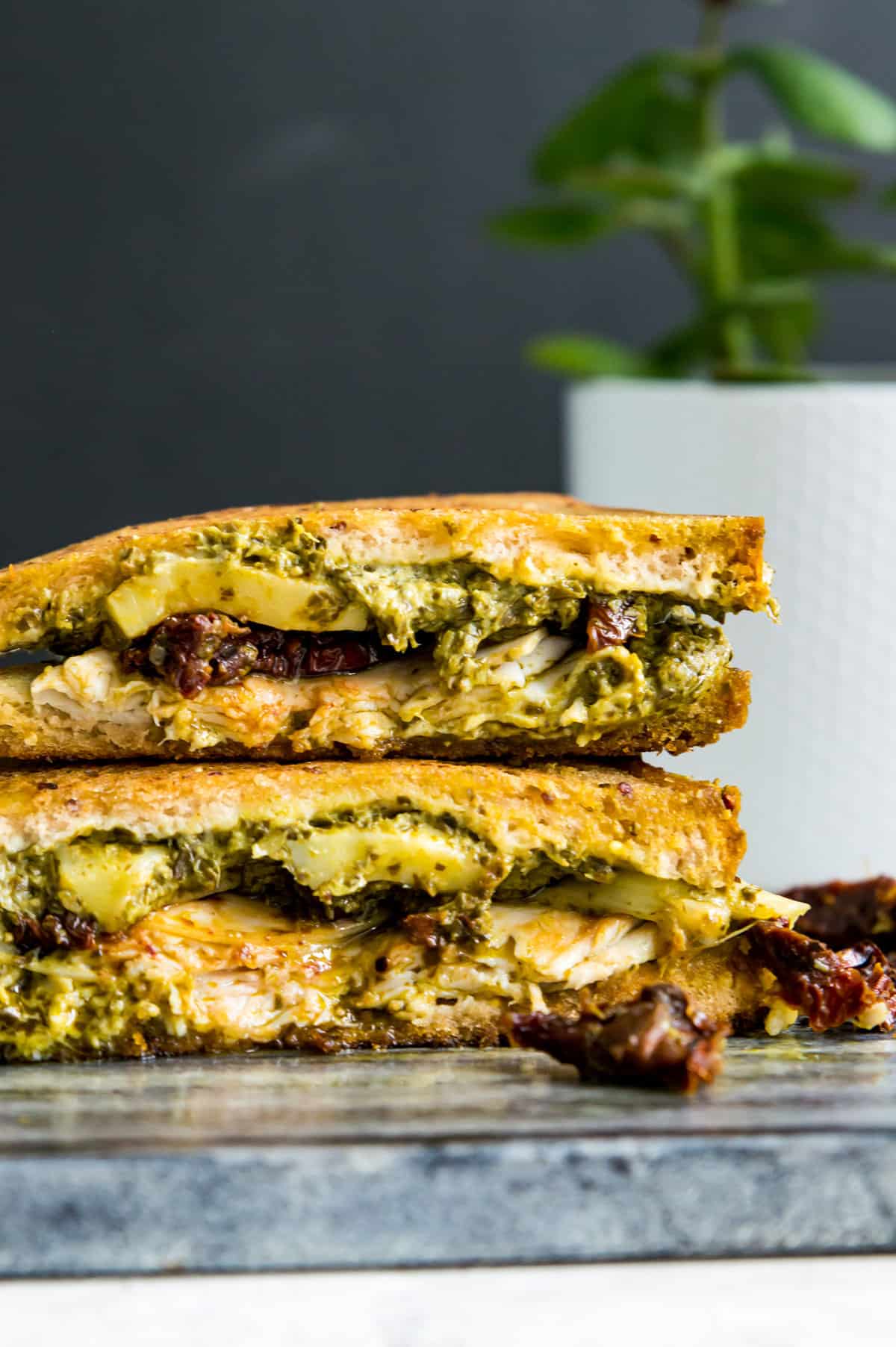 A stack of turkey pesto sandwich with cheese, sun-dried tomatoes, turkey and bread.
