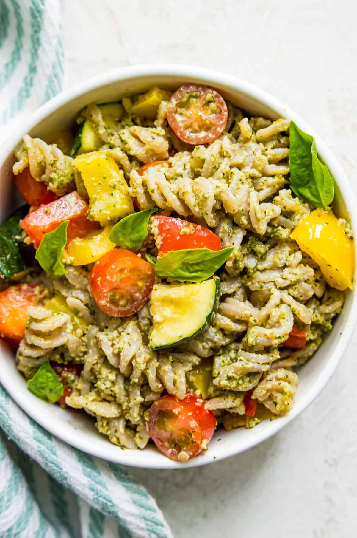 A bowl of veggie pesto pasta topped with fresh basil leaves.