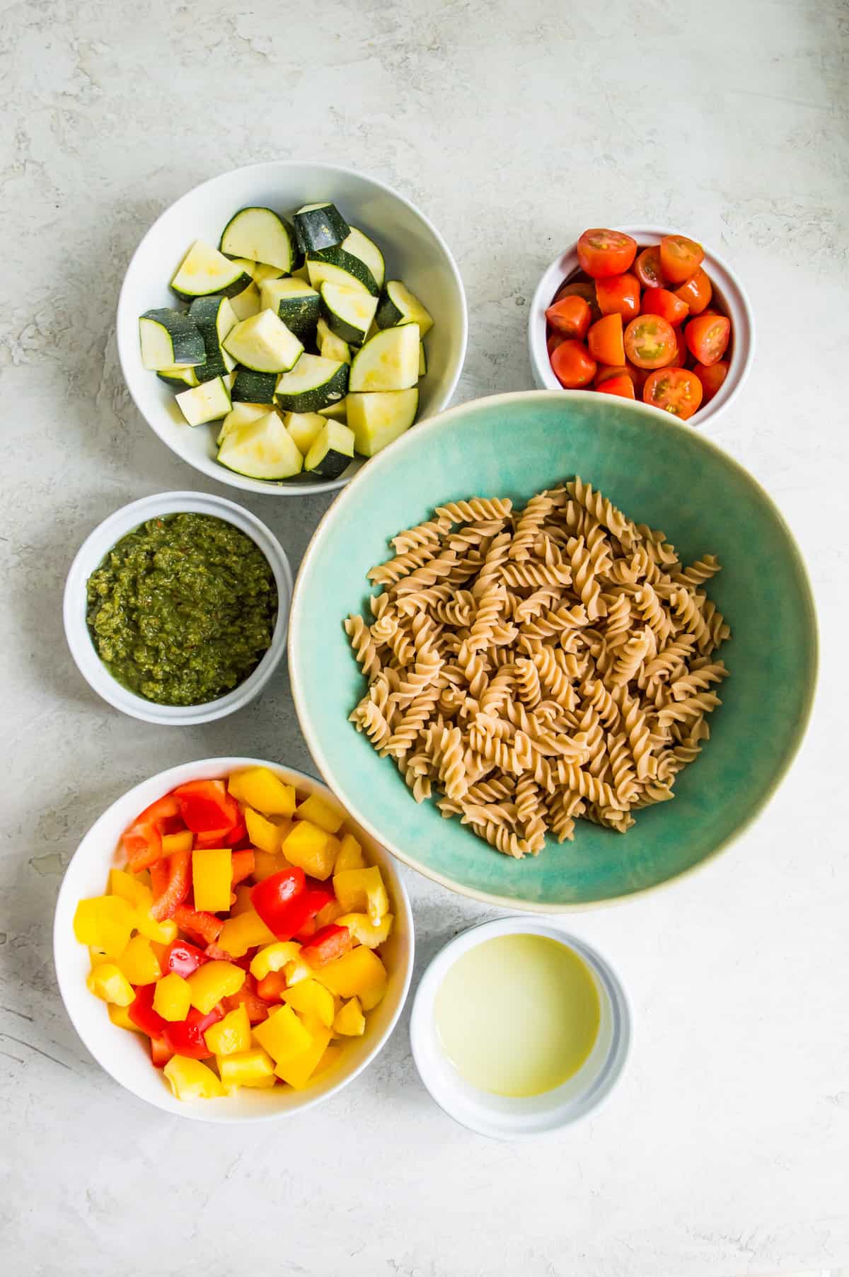 The ingredients needed to make veggie pesto pasta separate in to small bowls.