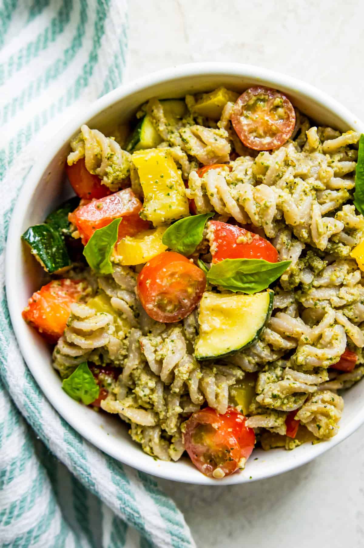 A bowl of pesto pasta topped with vegetables and fresh basil.