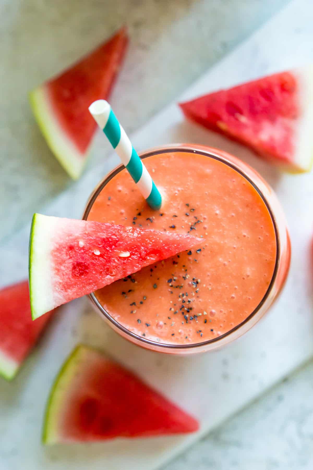 A watermelon banana smoothie in a glass with a straw and a piece of watermelon on top.