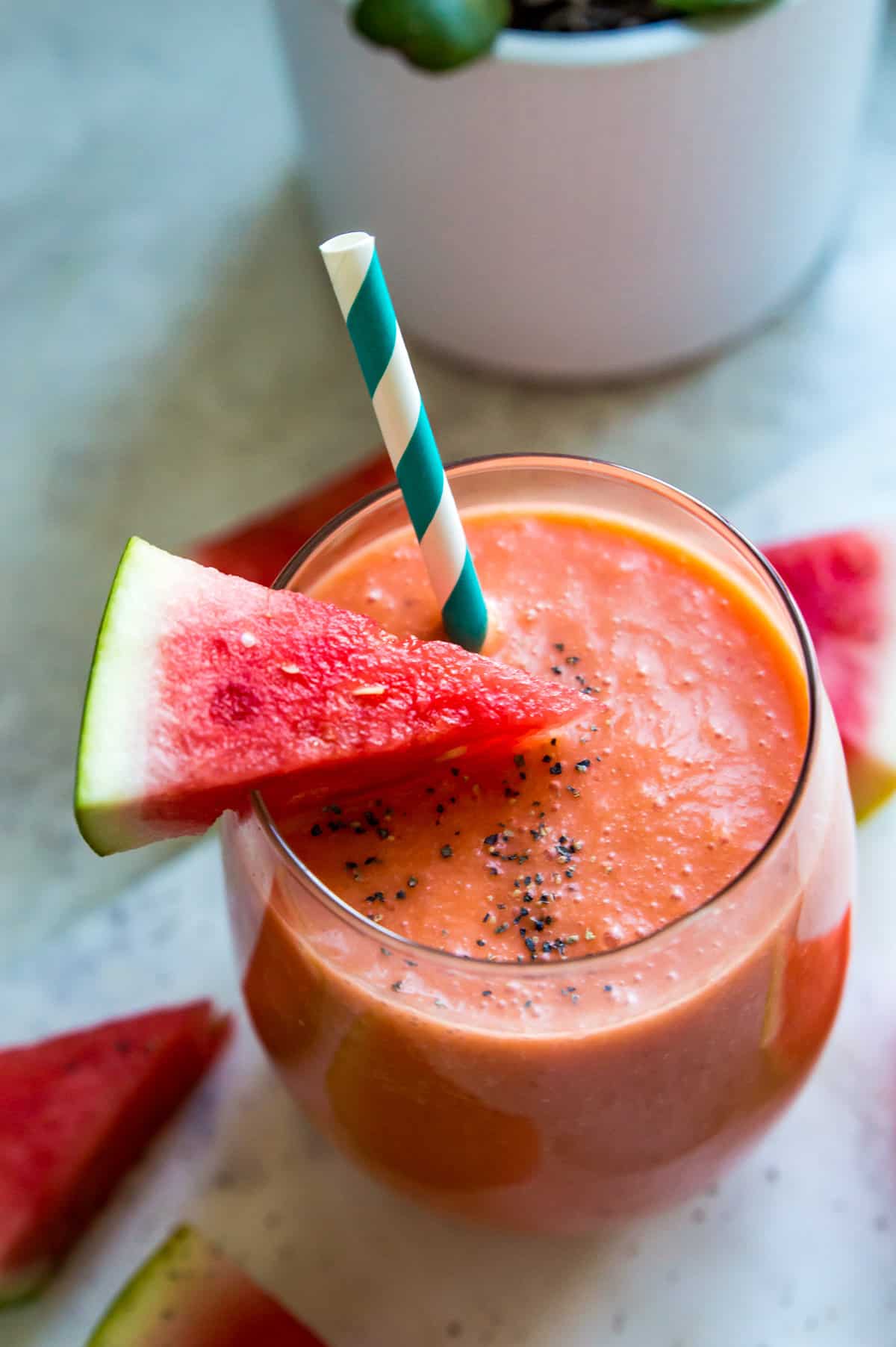 A watermelon banana smoothie in a glass with a straw and a small piece of watermelon on top.