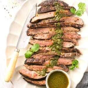 A cut bavette steak on a platter with chimichurri sauce on top.