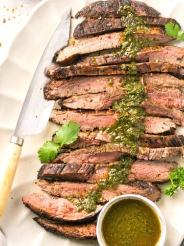 A cut bavette steak on a platter with chimichurri sauce on top.