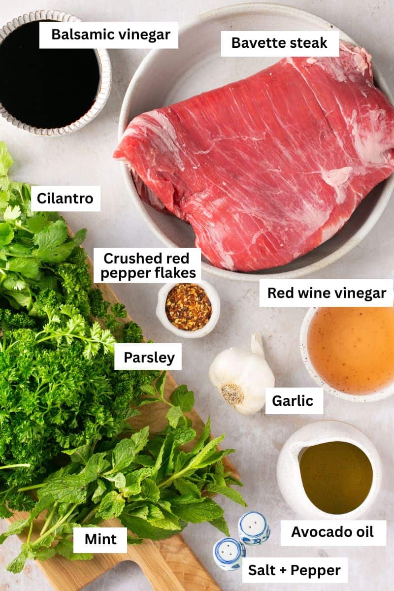 A piece of uncooked steak in a bowl surrounded by fresh herbs and spices.